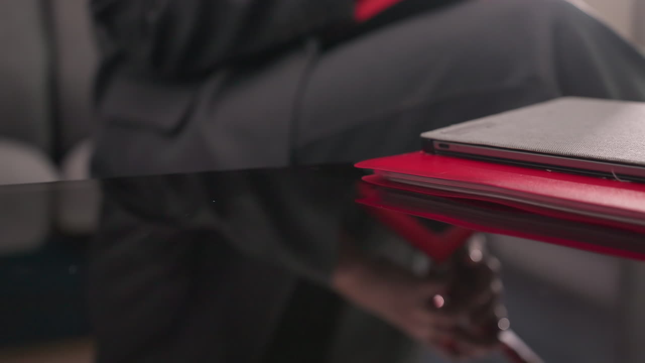 Close-up of red smartphone on top of red notebooks and laptop on glossy desk in office setting. Focus on work tools, productivity, and organized corporate workspace