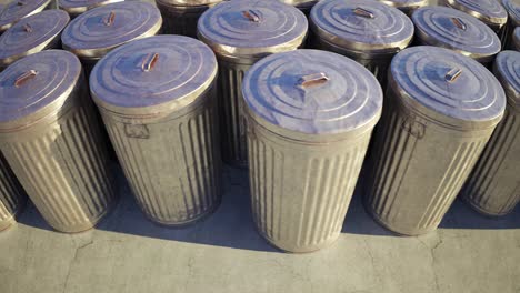 Steel-trash-bins-stacked-together-in-an-endless-loop.-Sunlight-illuminates-shiny-metal-lids-on-a-vast-field-full-of-containers-with-garbage-waste.-Symbol-of-growing-pollution-and-rubbish-outgrowth.