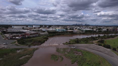 Brown-River-flooding-over-a-road-with-broken-down-car,-aerial