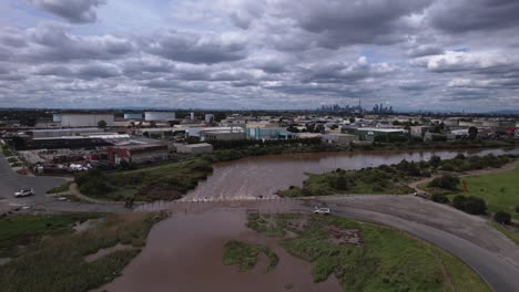 Río-Marrón-Inundando-Una-Carretera-Con-Un-Coche-Averiado,-Aéreo