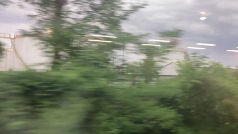 Factories-and-companies-in-the-Milanese-suburbs-in-Italy,-seen-from-the-train-window,-summer-evening,-cloudy,-livestock-and-pollution