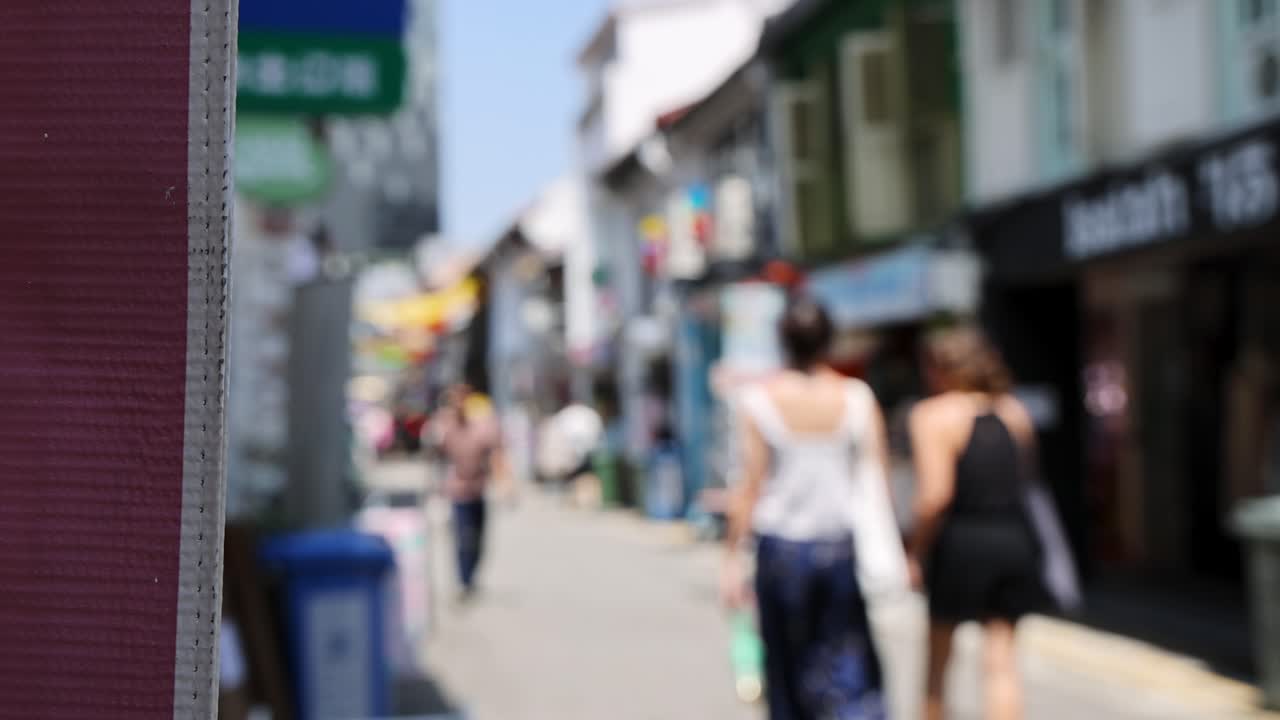 Two women stroll along vibrant outdoor shopping street, daylight, handheld camera, shallow focus
