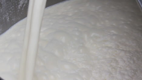 a close up view of milk filling in a container by pipe, making froth at the top, a little messy container by milk and a bit dirty pipe