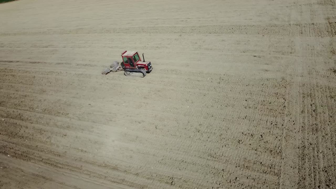 Aerial view of small tiny red tractor plowing preparing the land before the seeding, drone fly above agricultural land plantation growing organic biologic food