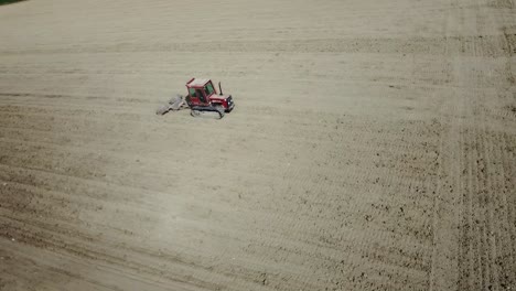 aerial view of small tiny red tractor plowing preparing the land before the seeding, drone fly above agricultural land plantation growing organic biologic food