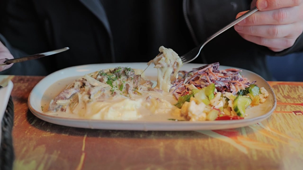 Person prepares to enjoy creamy beef stroganoff with mashed potatoes and fresh salads indoors.