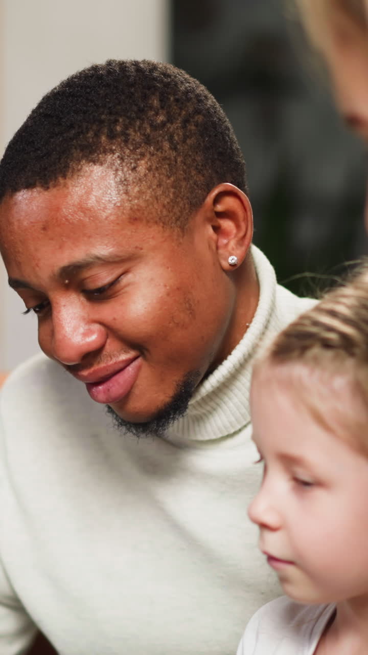 African-American bearded man groupmate nods looking at old pictures in album with woman friend and little girl in living room closeup slow motion