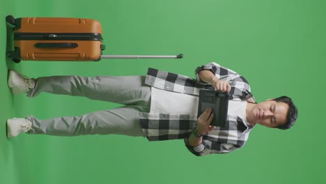 full body of asian male traveler with luggage using a tablet while standing in the green screen background studio