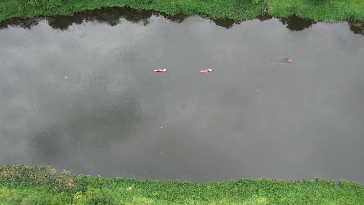 Hai chiếc thuyền kayak màu đỏ tươi trôi nhẹ nhàng xuôi dòng sông Neris ở Vilnius, nhìn từ trên cao với hình ảnh phản chiếu dịu nhẹ trên mặt nước