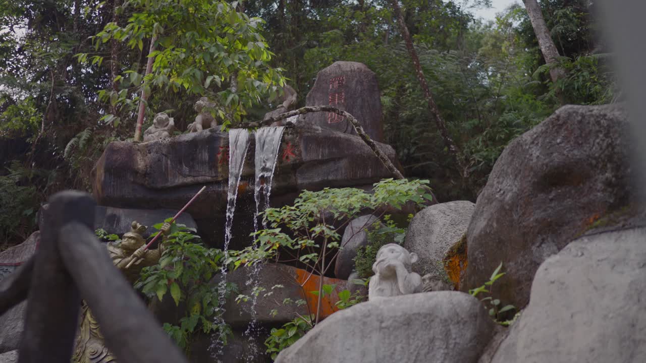 A tranquil waterfall flows in a lush forest, adorned with stone carvings of mythical figures. Tall trees surround as water cascades over rocks, creating a serene scene.