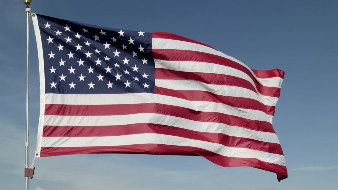 Waving American flag reacting to breeze on pole against clear sky showing stripes