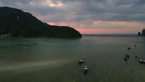 Schöner-Luftbildflug-über-Eine-Tropische-Insel-Bei-Sonnenuntergang-Und-Wolkigem-Himmel-Mit-Booten,-Die-Auf-Einem-Türkisfarbenen-Meer-Segeln