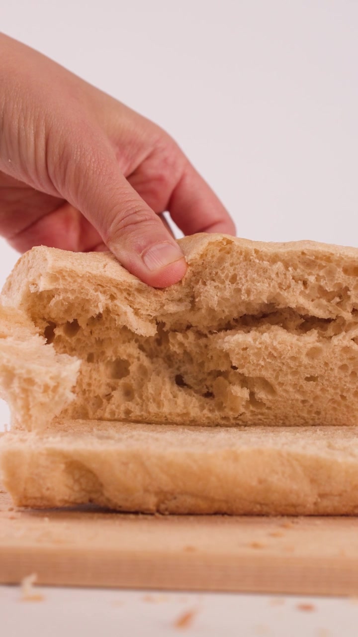 Close-up of hands pulling apart crusty bread on a wooden board against white background.