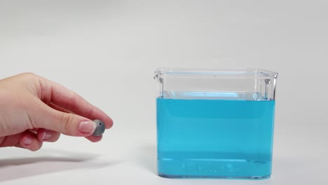 a lead ball is dropped into a clear container of blue liquid, demonstrating buoyancy and density principles