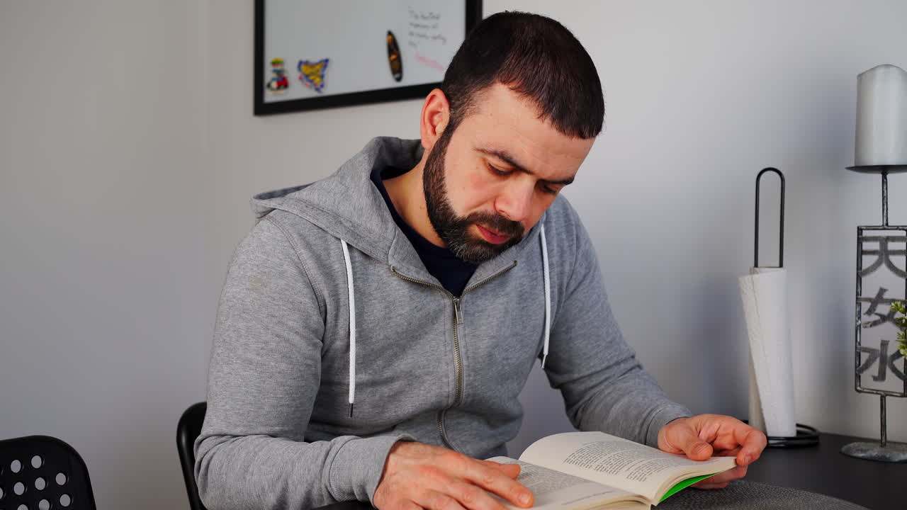 hombre barbudo leyendo un libro en la mesa de la casa
