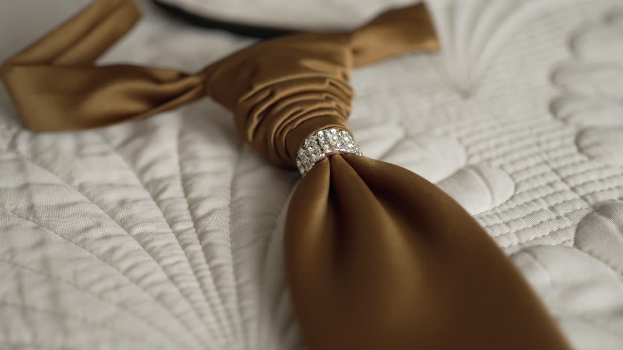 Close up of a satin tie with a crystal detail, lying on a quilted white surface