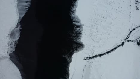 una hermosa toma de drones de la playa negra en islandia muestra las altas olas del mar y el clima nublado mientras la nieve cubre parte de la arena negra