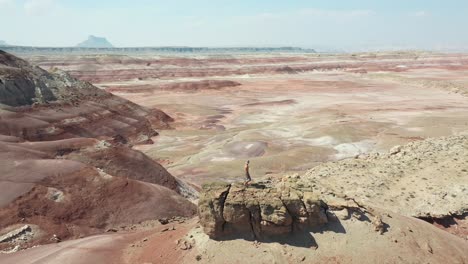 Vista-Aérea-De-órbita-Dinámica-De-Un-Hombre-Solitario-Caminando-Sobre-Una-Roca-En-La-Cima-De-Una-Colina-Sobre-El-Desierto-En-Utah,-Ee.uu.