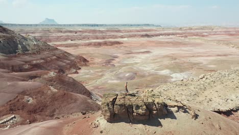 vista aérea de órbita dinámica de un hombre solitario caminando sobre una roca en la cima de una colina sobre el desierto en utah, ee.uu.