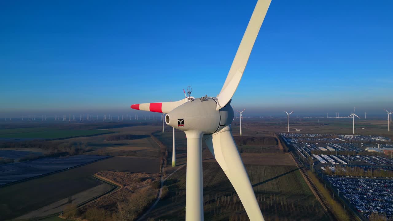 primo piano di una turbina eolica con molte turbine, pannelli solari e un parcheggio sullo sfondo sotto un cielo azzurro. Splendido panorama aereo con drone