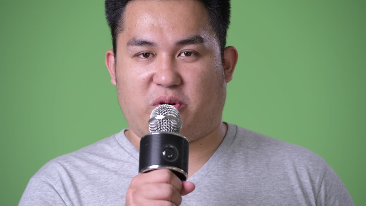 Young handsome overweight Asian man against green background