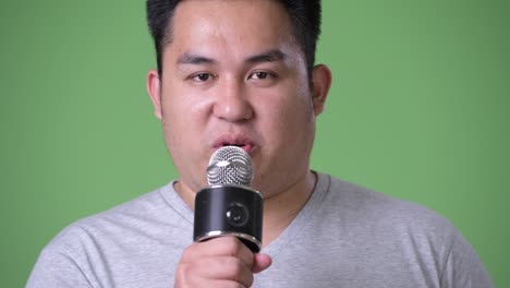 young handsome overweight asian man against green background