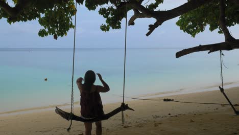 a woman sits on a wooden swing on a tropical beach and plays with her hair