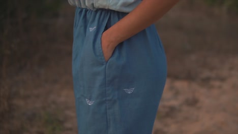 view of a young girl body on beach in a blue dress with her hands in her pockets, slow motion