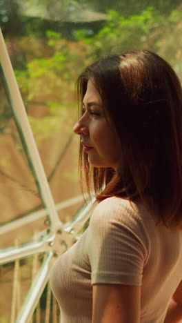 woman stands at window and looks out at woodland in distance. lady spends time on viewing platform above dense trees. female reposes communing with nature