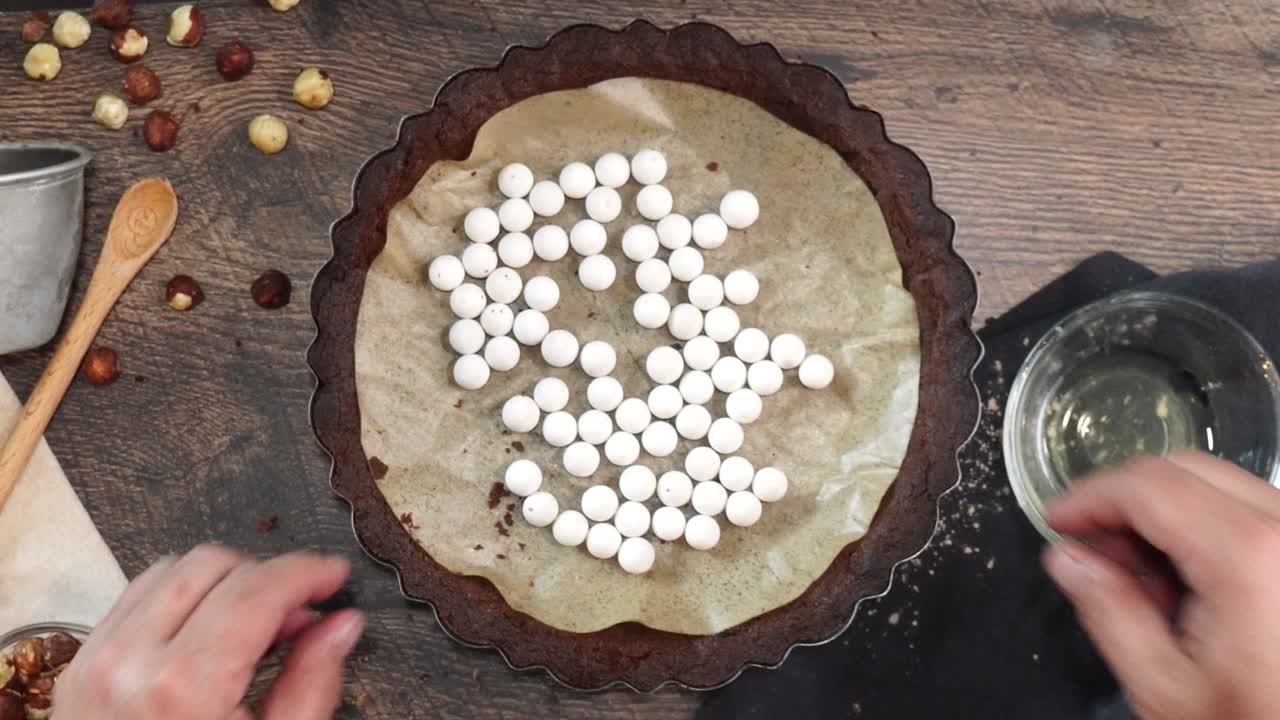 A delicious dessert, Coffee Hazelnut Cream Tart. Made with espresso powder, chocolate crust and loaded with crushed hazelnut. Removing white pie weights from the chocolate crust on a wooden table