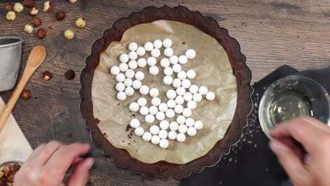 a delicious dessert, coffee hazelnut cream tart. made with espresso powder, chocolate crust and loaded with crushed hazelnut. removing white pie weights from the chocolate crust on a wooden table
