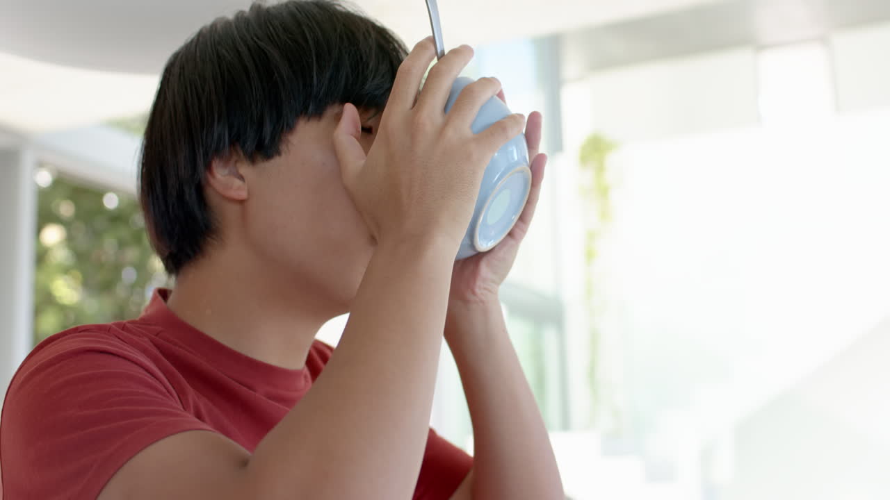 십대 아시아 소년 은 복사 공간 이 있는 집 의 밝은 부 에서 컵 에서 술 을 마신다