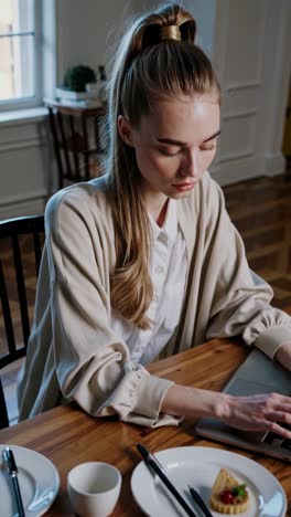 young woman works attentively on her laptop in a stylish, cozy home workspace. breakfast is set on the wooden table, suggesting a balanced work life environment