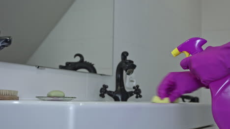 a woman in rubber gloves cleans the sink with a sponge and spray