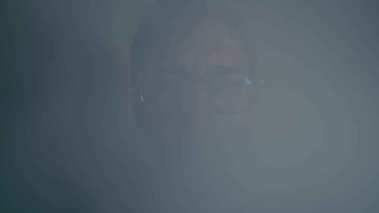 Young pimply man with red glasses vaping and exhales smoke in the camera. Smiling at the end. Close up. Slow motion