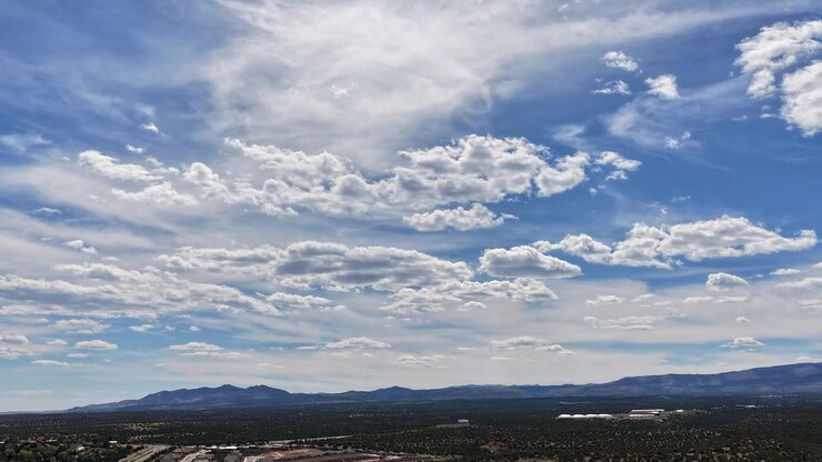 Un timelapse 4K de dron captura hermosas nubes blancas moviéndose por un cielo azul sobre un vasto horizonte montañoso. El movimiento atmosférico cinematográfico revela un paisaje accidentado del suroeste y una vista de desierto abierto.