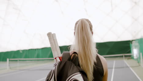 TRACKING-Young-Caucasian-female-tennis-player-entering-the-court,-rackets-in-a-backpack.-4K-UHD-RAW-graded-footage