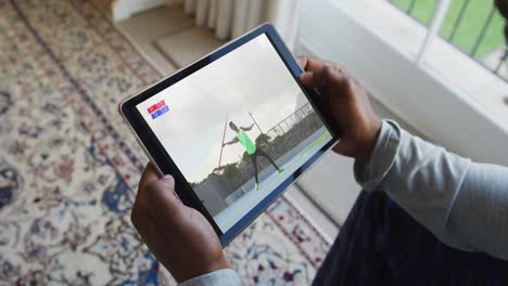 Compuesto-De-Un-Hombre-Sentado-En-Casa,-Viendo-Un-Evento-De-Jabalina-De-Atletismo-En-Una-Tableta