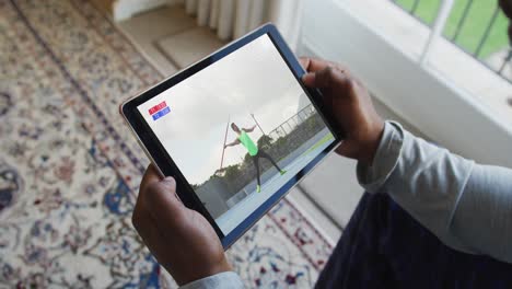 compuesto de un hombre sentado en casa, viendo el evento de jabalina de atletismo en la tableta