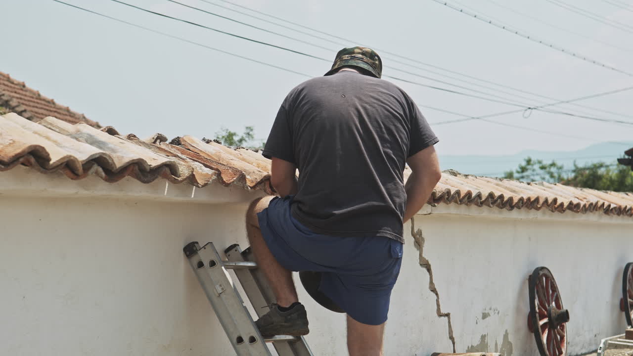 Man on ladder repairs terracotta tiled wall with cement and trowel slow motion