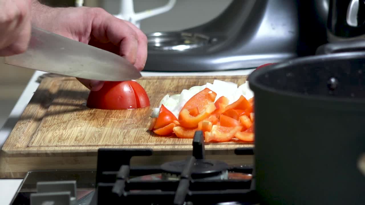 Men's hands cut tomatoes into large pieces. A male cook prepares vegetables for stew on a cutting board