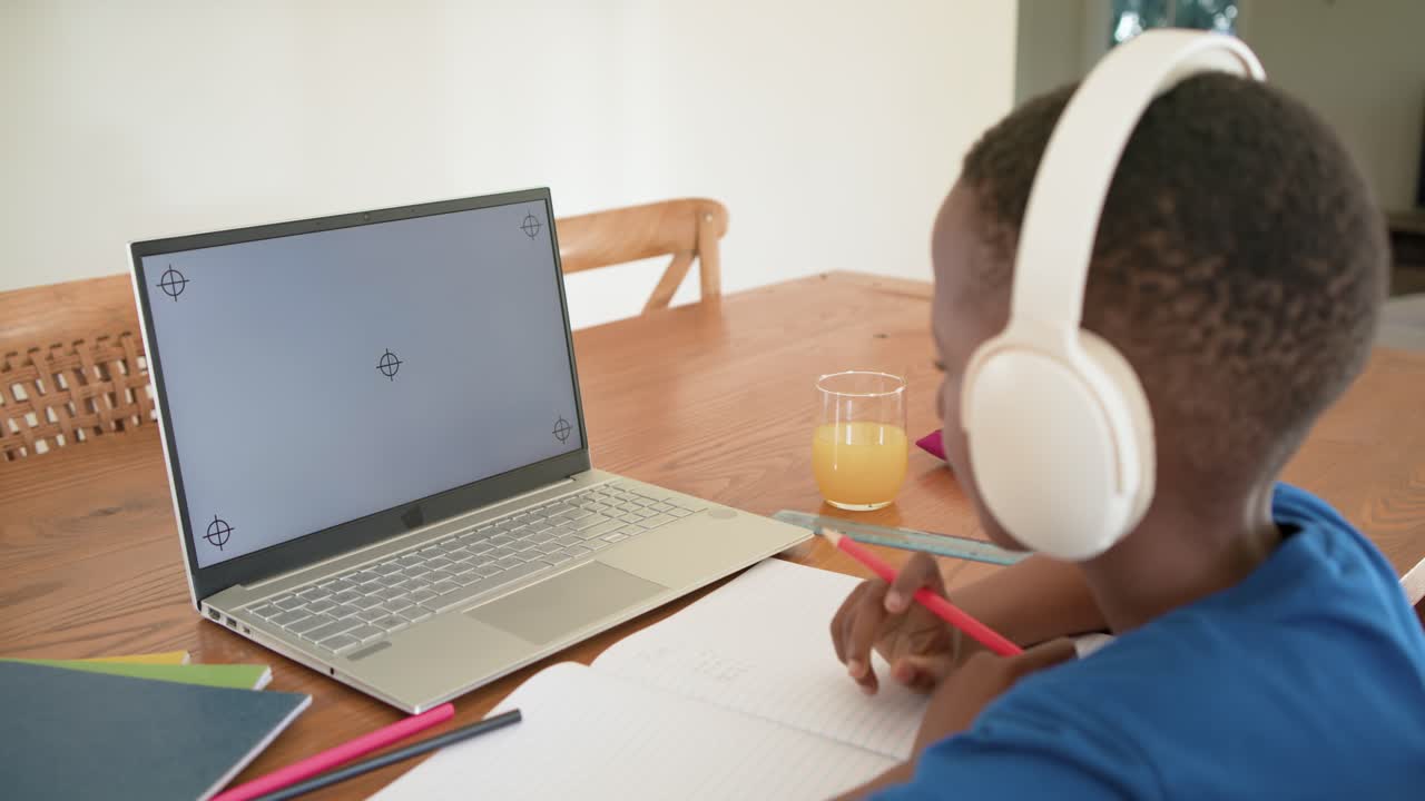 Student is placing red pencil on notebook on table, writing homework notes while checking laptop