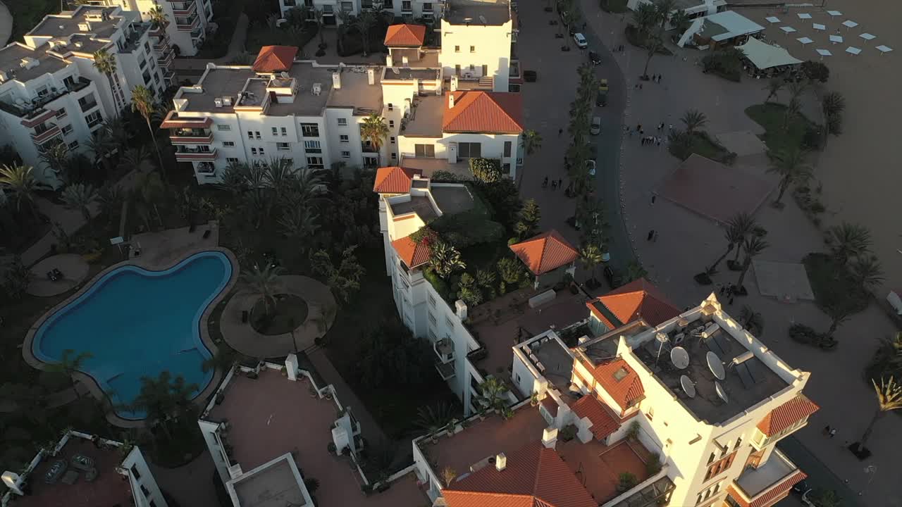 Aerial view looking down on Agadir hotel complex with swimming pool, streets, and rooftops at sunrise, Morocco