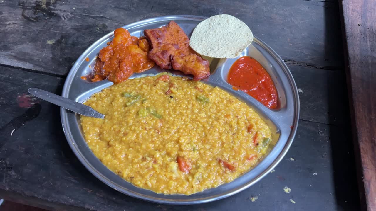 khichuri con alu dum, chutney y papad servido en un plato por un restaurante bengalí