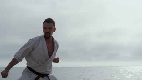 man making karate kicks on seacoast close up. athlete training fighting skills.