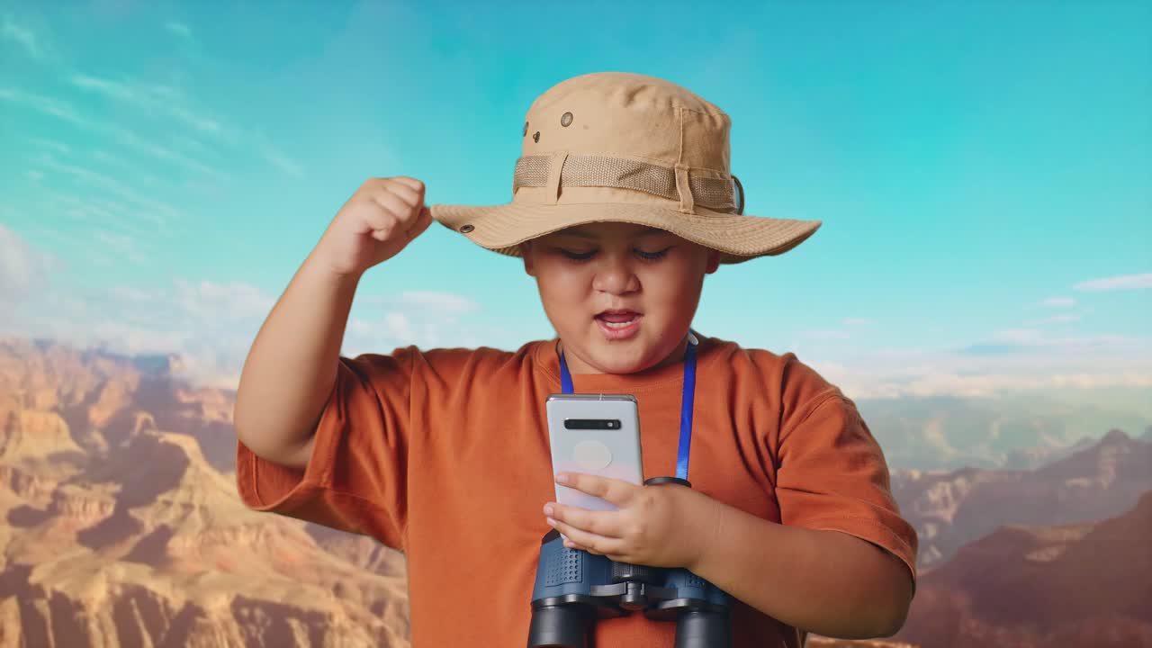 Asian Boy With A Hat And Binoculars Looking At Smartphone Then Screaming Goal Celebrating While Traveling At The Top Of Mountain. Boy Researcher Examines Something, Travel Tourism Adventure, Close Up