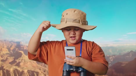 asian boy with a hat and binoculars looking at smartphone then screaming goal celebrating while traveling at the top of mountain. boy researcher examines something, travel tourism adventure, close up