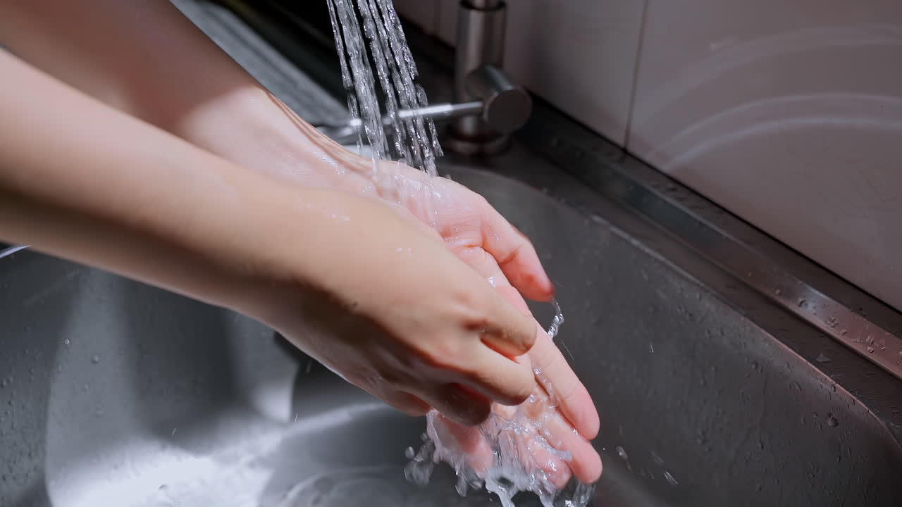 Hands of woman wash their hands in a sink with foam to wash the skin and water flows through the hands