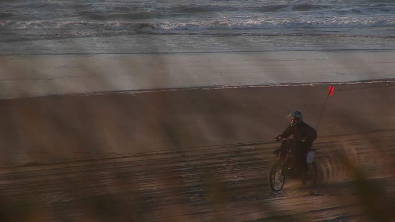 더트 바이커는 골든 아워 동안 모래 해변에서 트랙을 만듭니다.
