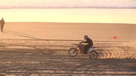 Un-Motociclista-Hace-Pistas-En-Una-Playa-De-Arena-Durante-La-Hora-Dorada.